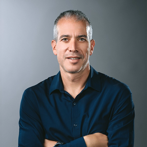 Middle-aged man with short gray hair wearing a dark shirt against a blue background with white dot pattern.