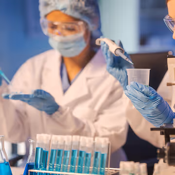 Scientists in protective gear working with blue liquid in test tubes and a pipette in a laboratory.