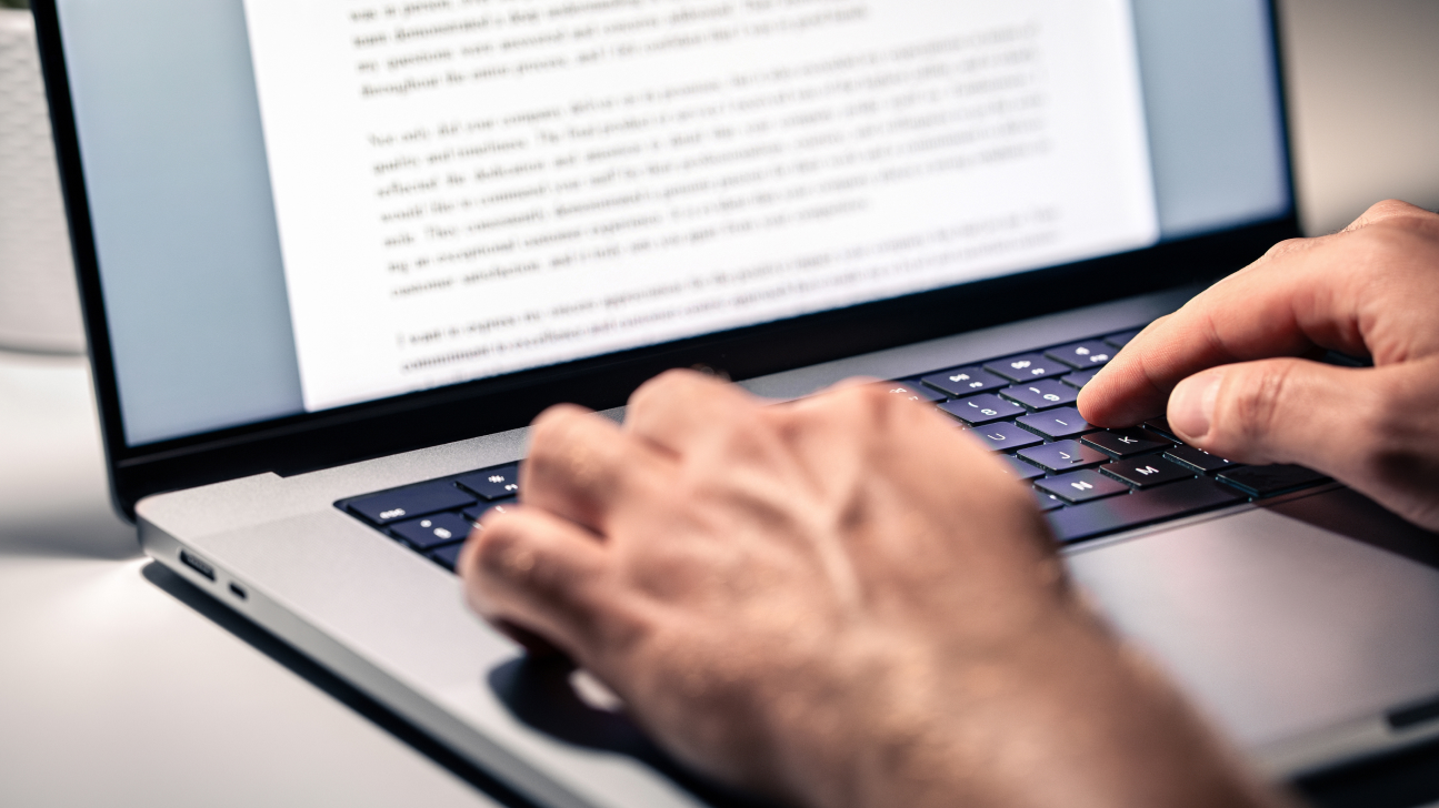 A person types words into a document on their laptop.